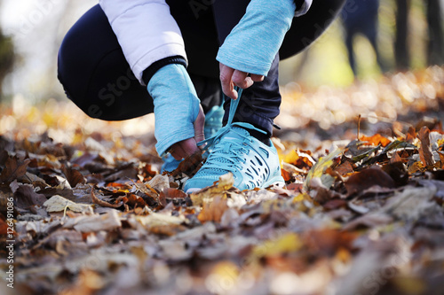Woman tying shoelaces before start running , runner close up in a autumn forest sport and lifestyle concept