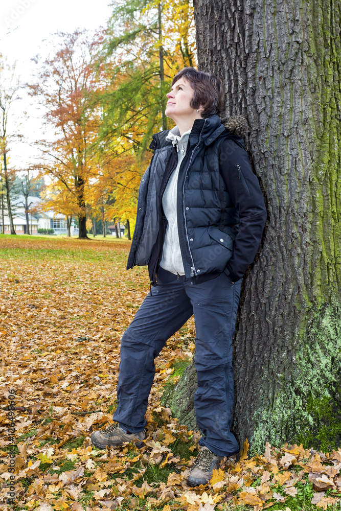 Woman leans in the tree and enjoys the autumn wood