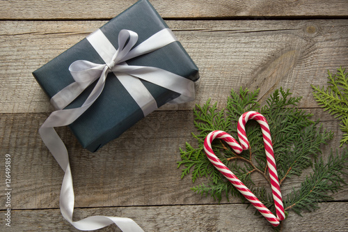 Handmade chistmas present from black wrapping paper, silver ribbon and candy cane in shape of heart on wooden surface. Top view and copyspace.