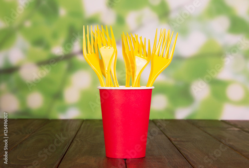 Bright disposable paper cup and plastic forks on abstract green.