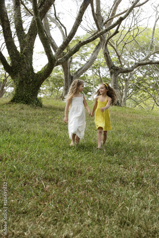 two girls holding hands, skipping in woods