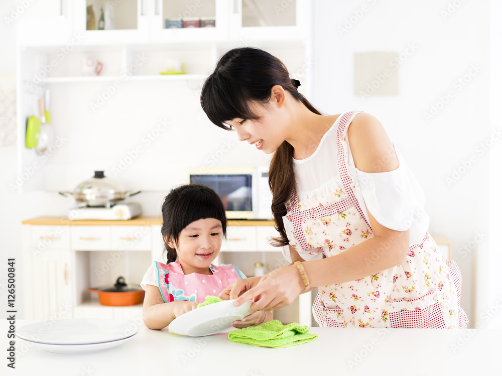 little girl helping her mother clean dish in the kitchen