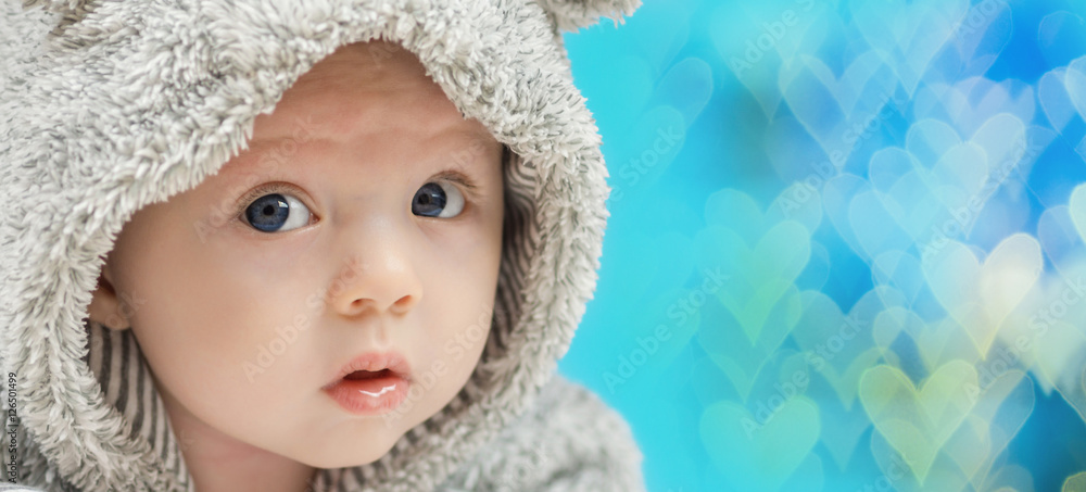 closeup of beautiful happy baby with blue eyes in grey bear like clothing on blue heart shaped background closeup of beautiful happy baby with blue eyes in grey bear like clothing on blue heart shaped background