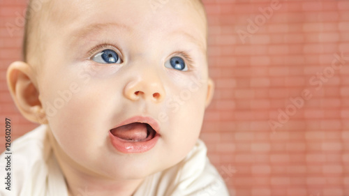 closeup of beautiful happy baby with blue eyes on red brick background