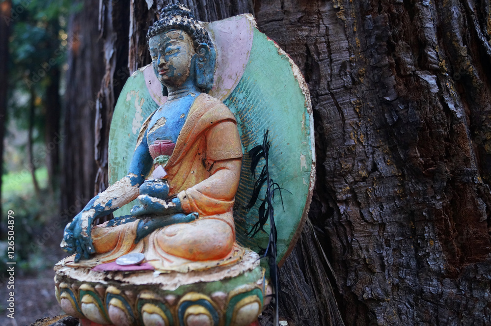 Bunter Buddha sitzt vor einem Baumstamm und meditiert.