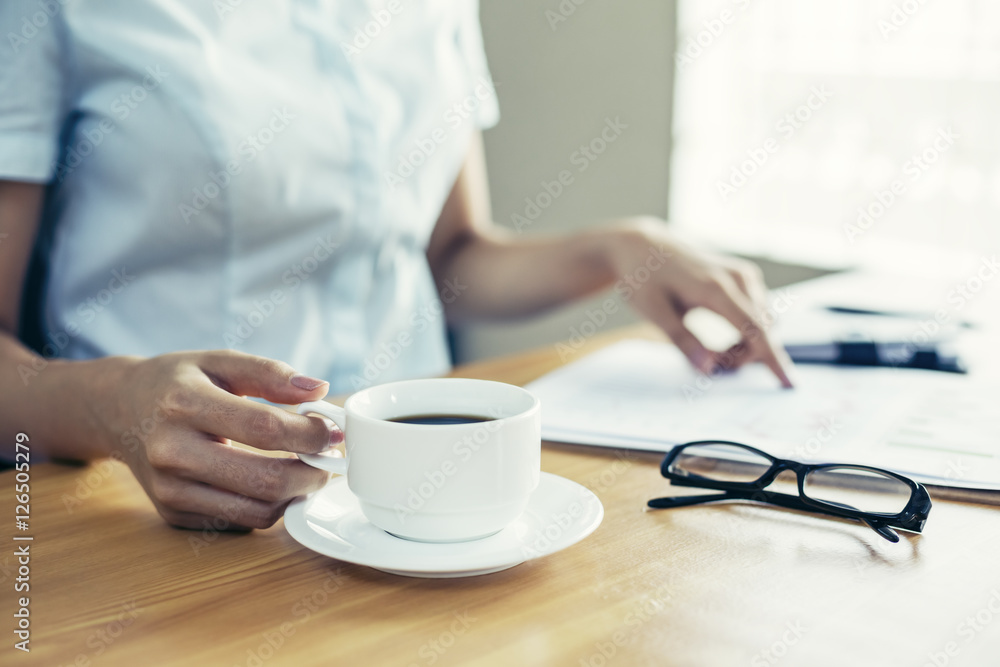 businesswoman indoor reading document on her desk and holding coffee cub businesswoman indoor reading document on her desk and holding coffee cub