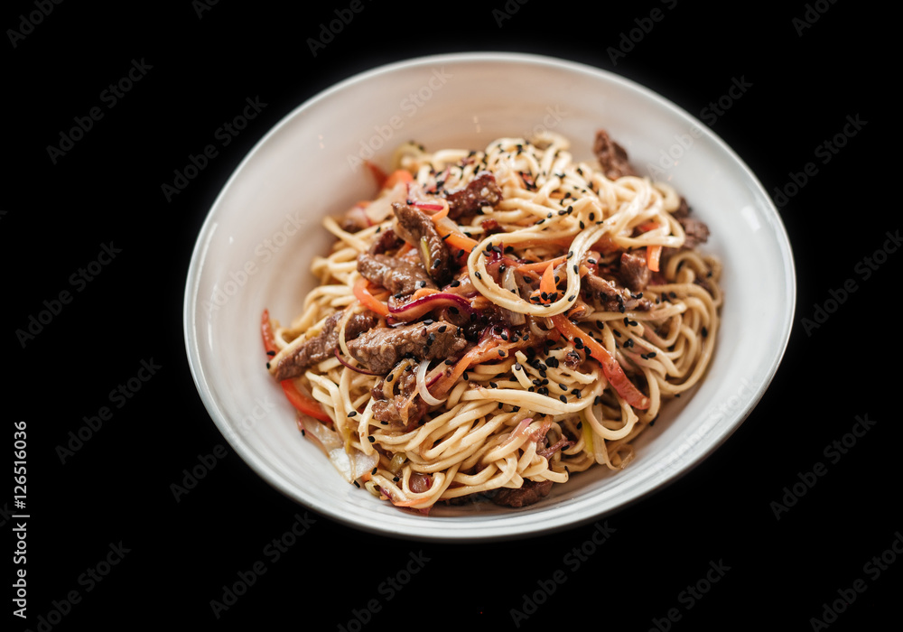 Egg noodles with beef and vegetables in a white plate on a black background. Healthy Asian cuisine. Side view.