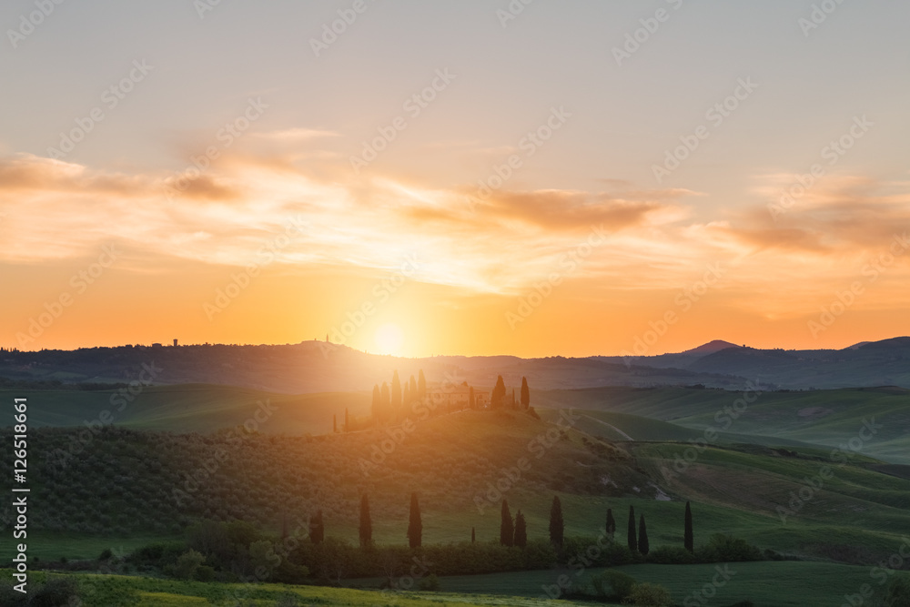 Farmhouse, green hills,cypress trees in Tuscany at sunset