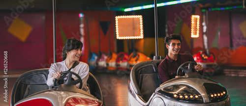 Foto Two young friends riding bumper cars at amusement park