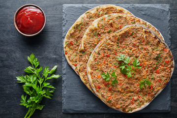 Lahmacun traditional turkish pizza with minced beef or lamb meat, paprika tomatoes, parsley baked spicy food on dark table background