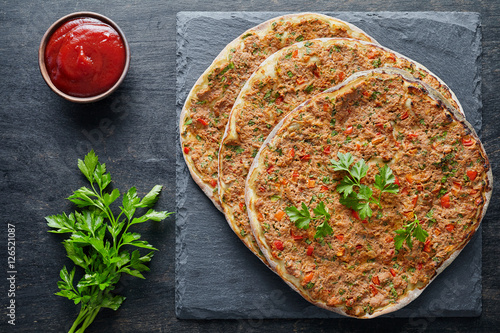 Lahmacun traditional turkish pizza with minced beef or lamb meat, paprika tomatoes, parsley baked spicy food on dark table background