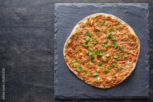 Lahmacun turkish gourmet pizza with minced beef or lamb meat, paprika, tomatoes, cumin spice, parsley baked spicy middle eastern food on dark table background