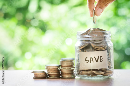Fototapeta Hand putting Coins in glass jar for money saving financial