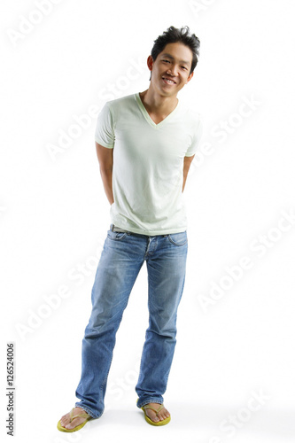 Young man in T-shirt and jeans, standing, smiling at camera