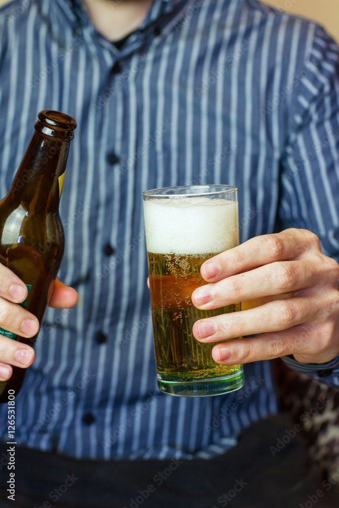 Hombre joven sirviendo una caña de cerveza con un vaso en una mano y un  botellín en la otra Stock Photo