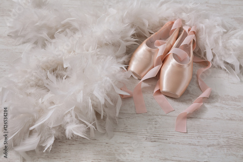 Pink ballet pointe shoes and feather on white wood background