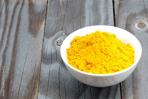 Turmeric powder in white cup on wooden floor.