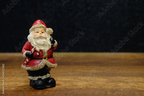 Santa claus statue and brown pine cone on wooden table with blac