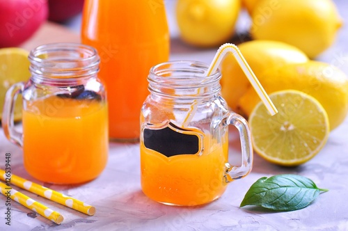 Delicious lemon mango juice in jar and bottles with straws.