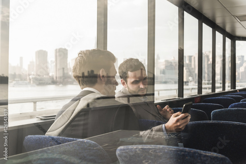 Two businessmen with cell phone talking on passenger deck of a ferry photo