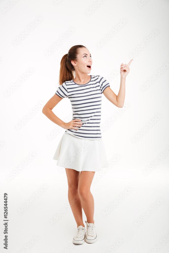Cheerful young woman in skirt standing and pointing finger away Cheerful young woman in skirt standing and pointing finger away