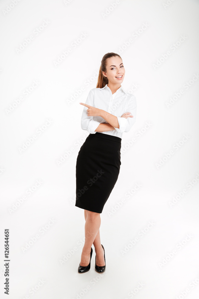 Cheerful young businesswoman pointing finger away and looking at camera Cheerful young businesswoman pointing finger away and looking at camera