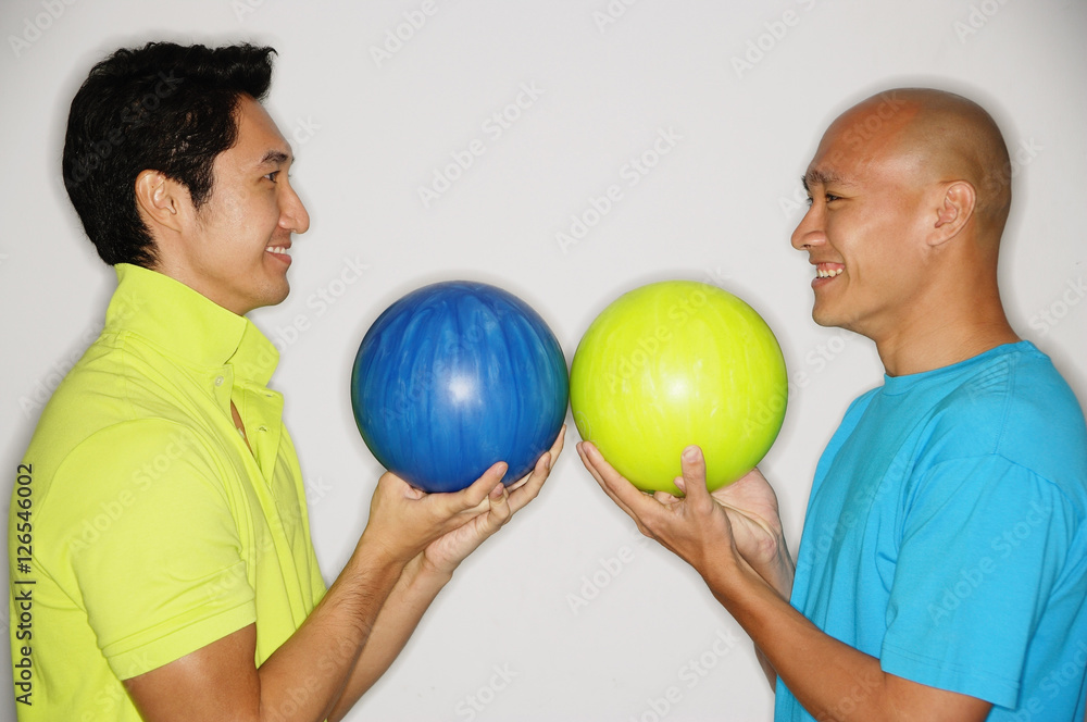 Two men standing face to face, carrying bowling balls, smiling Two men standing face to face, carrying bowling balls, smiling