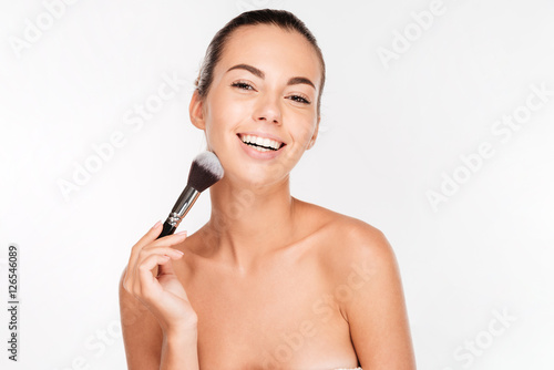 Smiling beautiful woman applying blush on face with brush tool