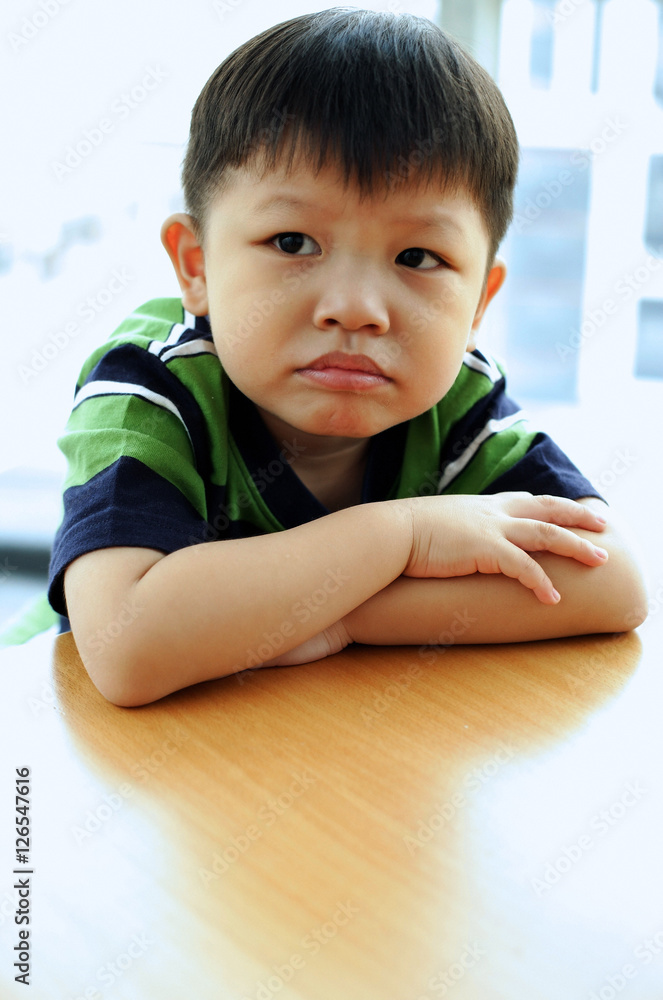 Young boy looking away, arms crossed, leaning on table Young boy looking away, arms crossed, leaning on table