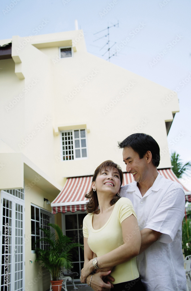 Fototapeta premium Couple standing in front of house, embracing