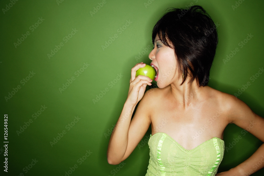 Woman biting into green apple, side view