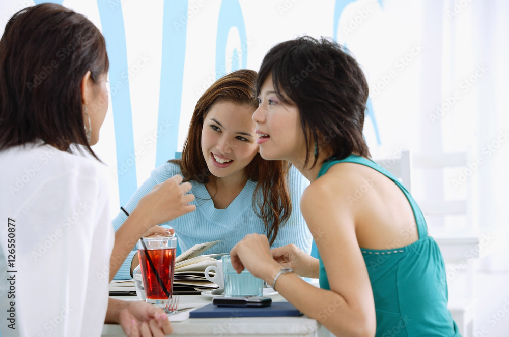 Fototapeta premium Three young women sitting in cafe, talking