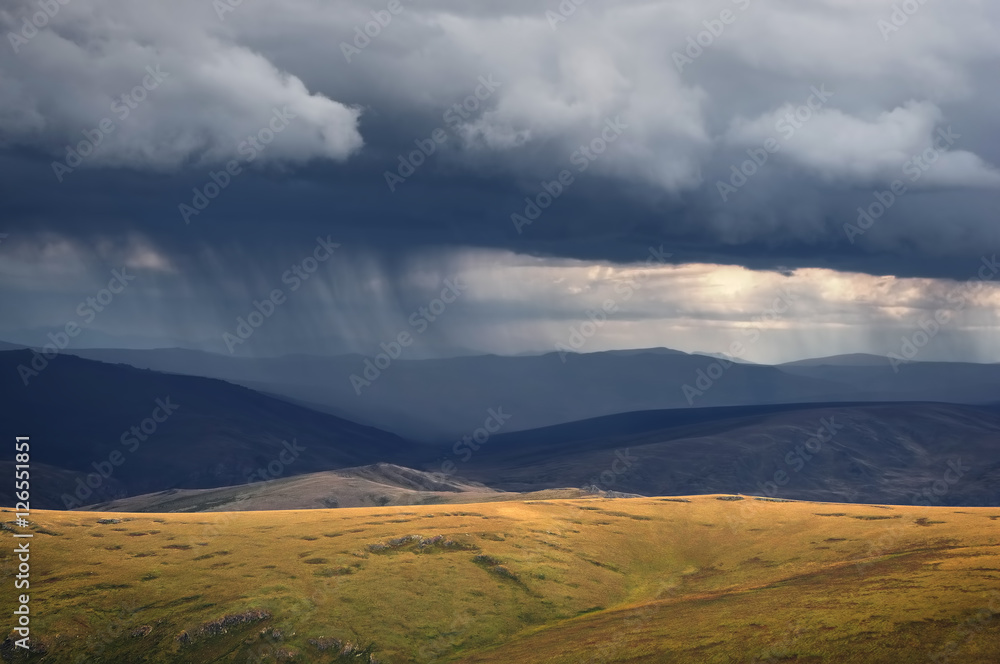 Rain from the storm dramatic dark scary clouds and a highland bright steppe with rocks in the foreground Plateau Ukok Altai mountains, Siberia, Russia