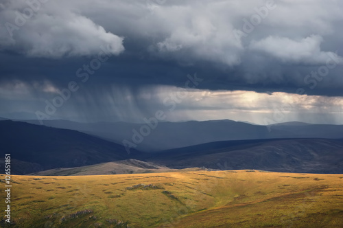 Rain from the storm dramatic dark scary clouds and a highland bright steppe with rocks in the foreground Plateau Ukok Altai mountains, Siberia, Russia