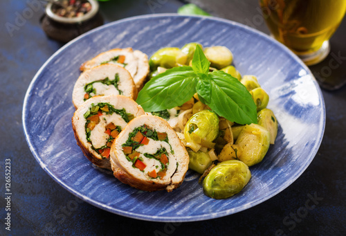 Chicken rolls with greens, garnished with stewed Brussels sprouts, apples and leeks on a blue plate.