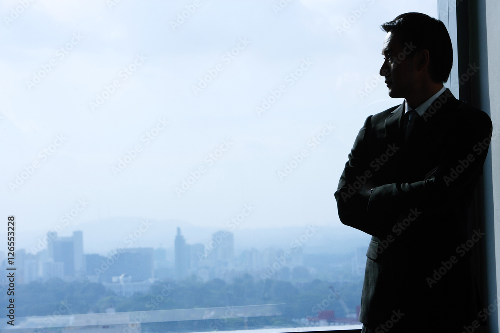 Businessman standing next to window, looking out Businessman standing next to window, looking out
