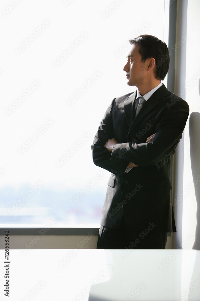 Businessman standing next to window, looking out, side view