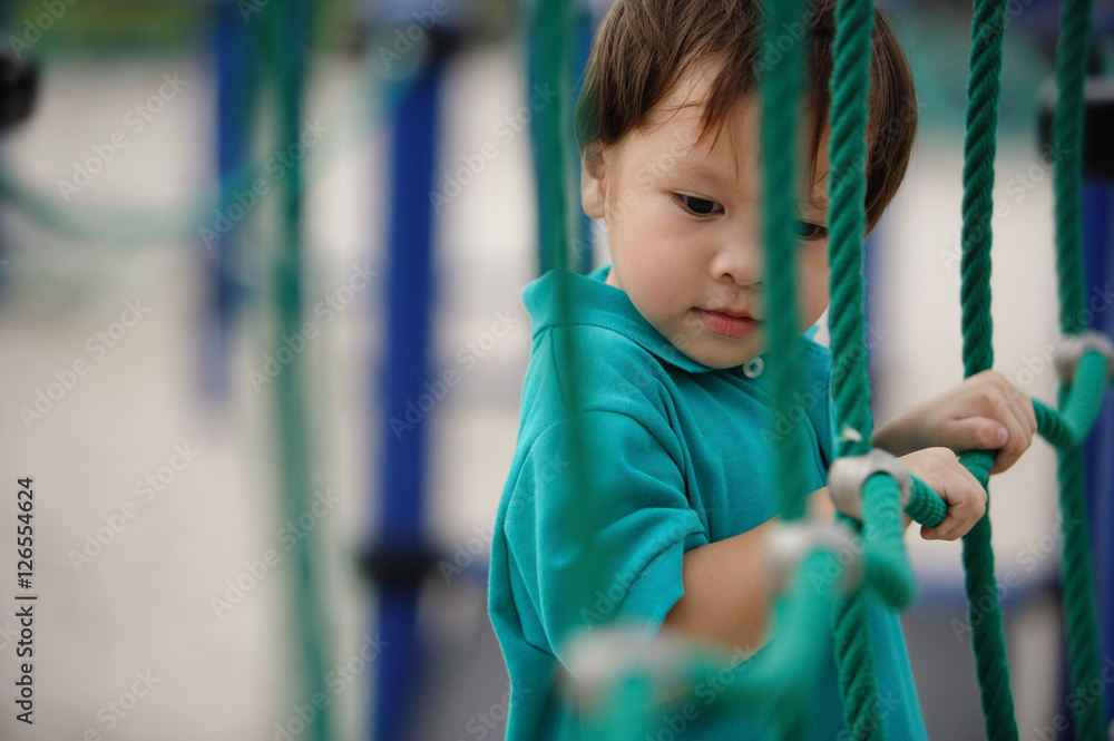 Young boy in playground, holding on to rope net