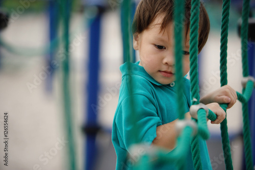 Obraz na płótnie Young boy in playground, holding on to rope net w salonie