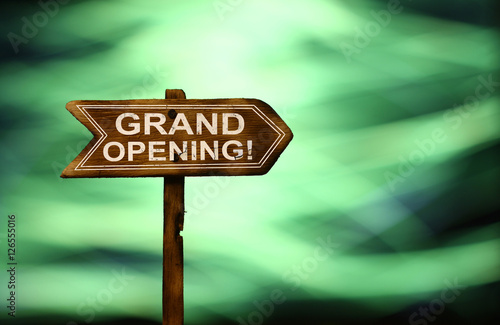 Obraz na plátně Old wooden arrows road sign with Grand Opening text white paint on colorful bokeh background