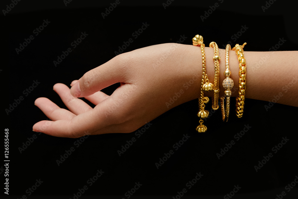 woman's hand with many different golden bracelets on black backg - obrazy, fototapety, plakaty 