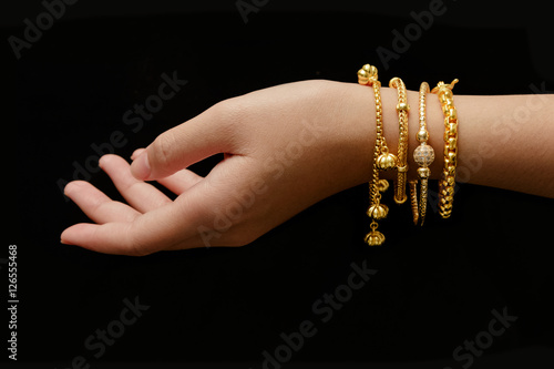 Fototapeta woman's hand with many different golden bracelets on black backg