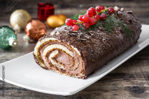 Chocolate yule log cake with red currant on wooden background


