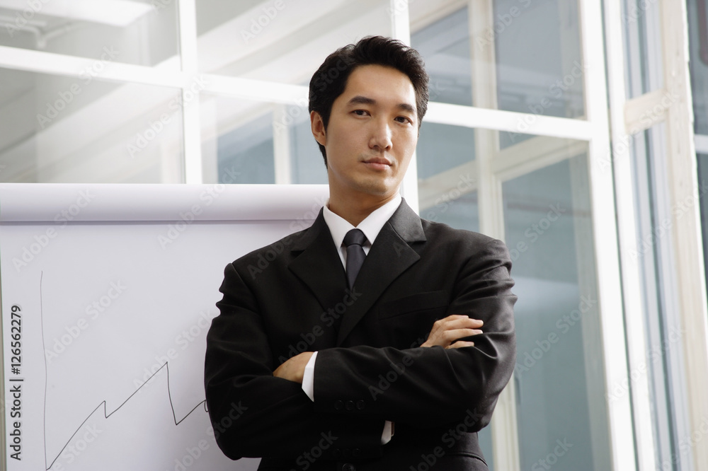 Businessman standing next to flipchart, looking at camera Businessman standing next to flipchart, looking at camera