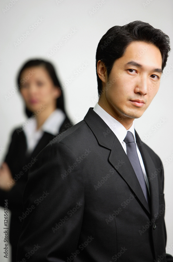 Businessman looking at camera, woman in the background Businessman looking at camera, woman in the background