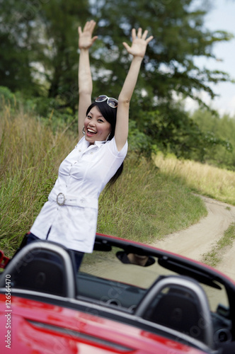 Woman standing in red sports car with arms raised