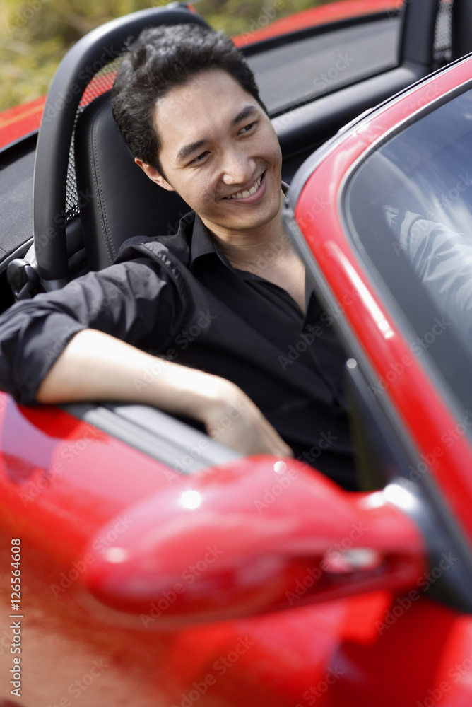 Man sitting in red convertible car, smiling
