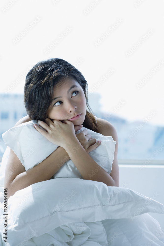 Young woman on bed, embracing pillow, looking away Young woman on bed, embracing pillow, looking away