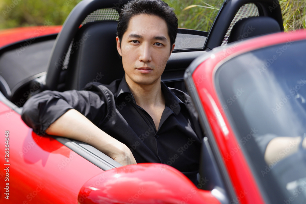 Man sitting in red convertible car, looking at camera, portrait