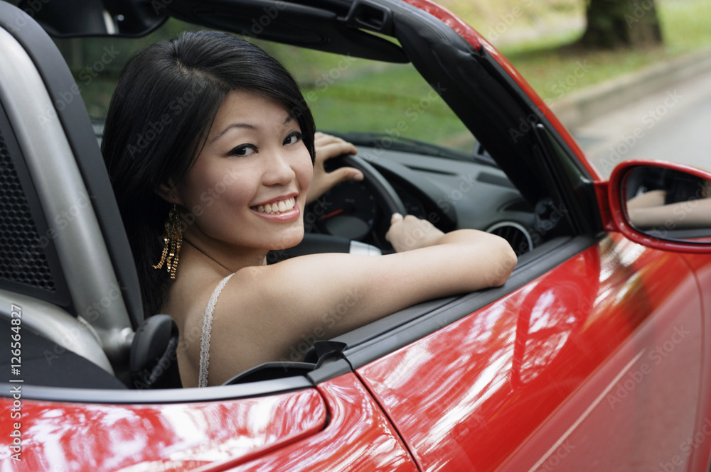 Woman driving red sports car, turning to smile at camera Woman driving red sports car, turning to smile at camera